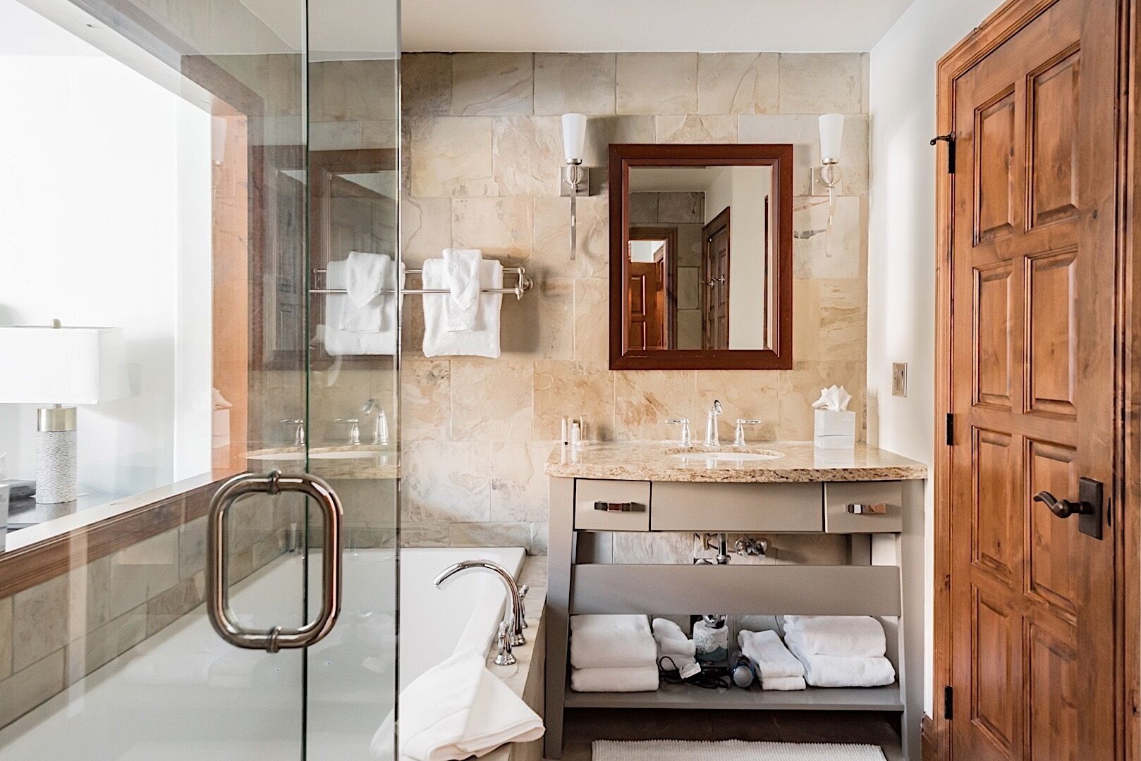 Un baño moderno con cabina de ducha de vidrio, tocador con mosaicos de mármol y puerta de madera.