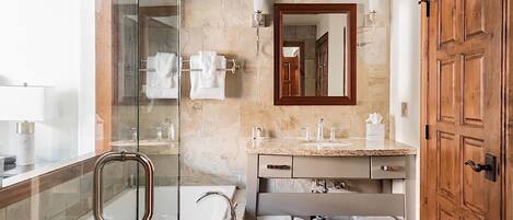 Un baño moderno con cabina de ducha de vidrio, tocador con mosaicos de mármol y puerta de madera.