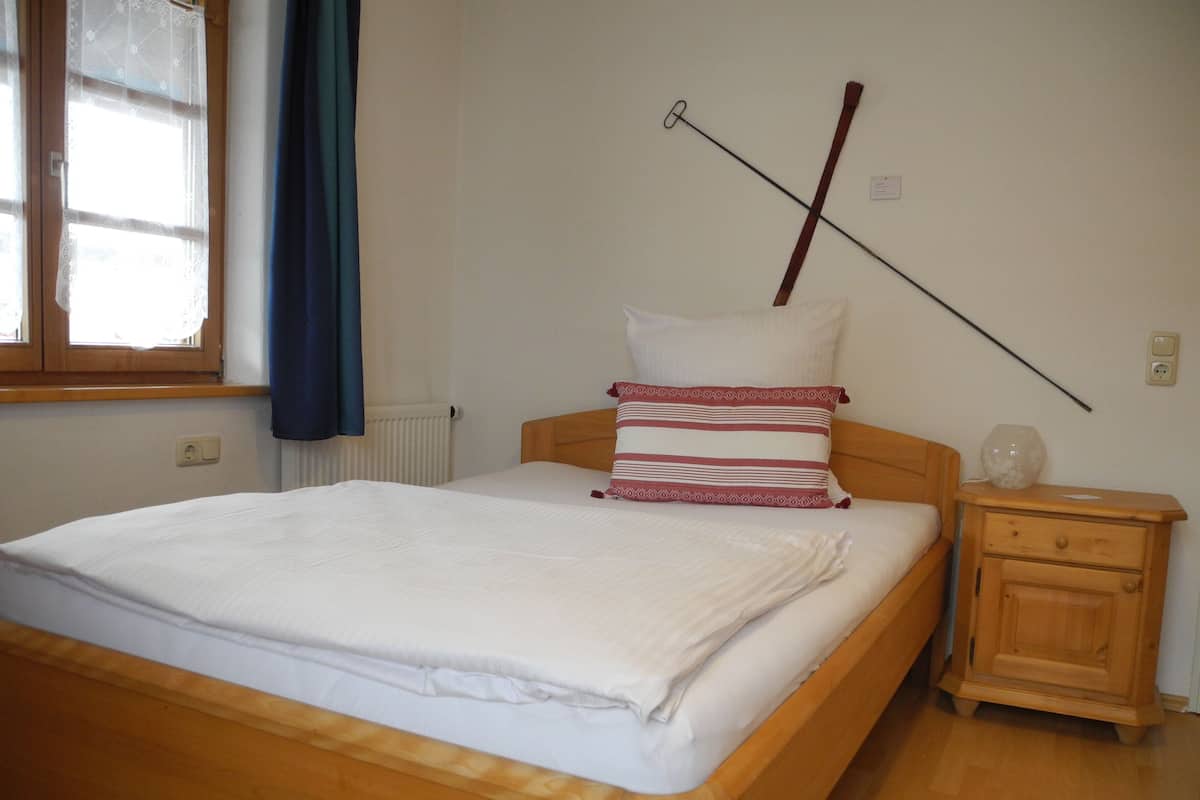 A neatly made bed with white bedding, a wooden headboard, and a bedside table with a lamp and a decorative vase.