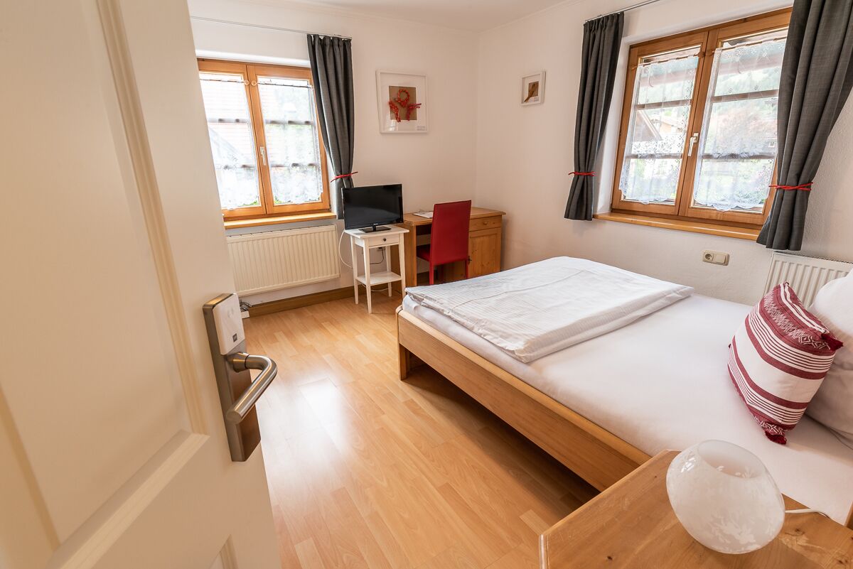 Een slaapkamer met een houten bed, een bureau met een computer, een stoel en een raam met gordijnen.