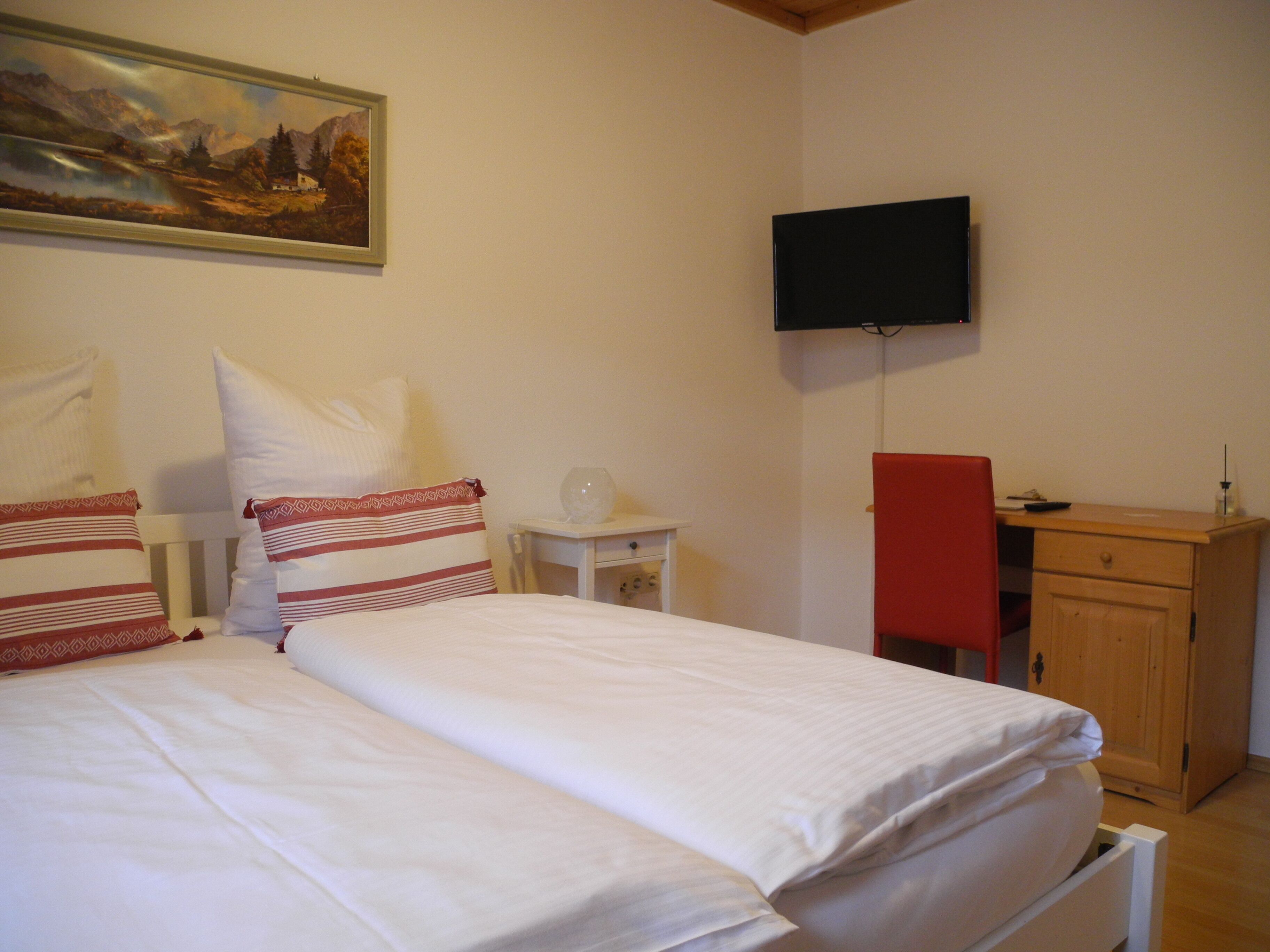Un dormitorio con dos camas, un televisor montado en la pared, un escritorio de madera y una pequeña mesa con un objeto de vidrio.