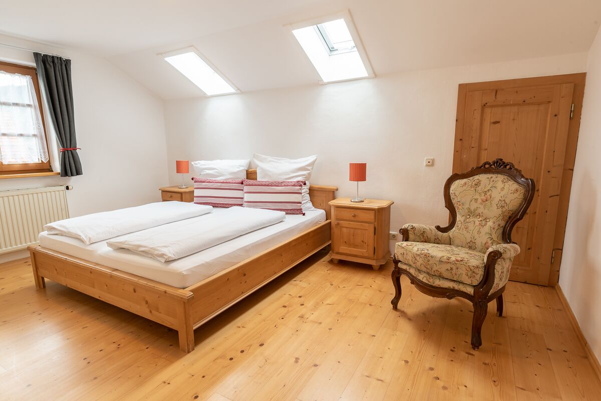Un dormitorio con una cama de madera, dos mesitas de noche con lámparas, una silla y un armario de madera.