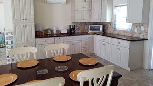 Una cocina con armarios blancos, microondas y una mesa de comedor con sillas.
