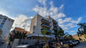 A multi-story residential building with balconies, parked cars, and a clear sky. - Location10 (Palermo)