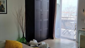 A modern bedroom with a bed, a wardrobe, a green vase with branches, and a view of the outside through a sliding door. - Location10 (Palermo)