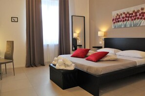 A hotel room with a bed, a chair, a bedside table with towels, a large painting, and a mirror. - Location10 (Palermo)