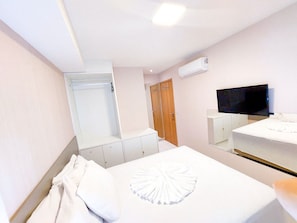Una habitación de hotel con cama, televisión, armario y espejo.
