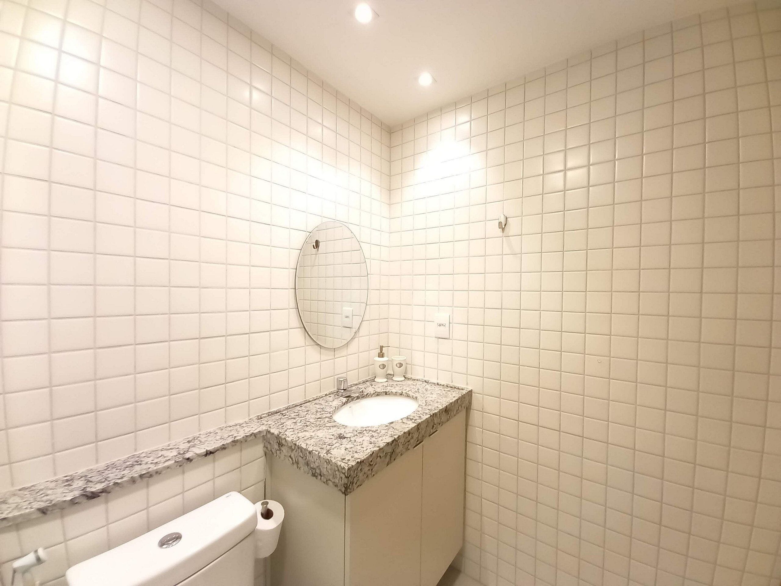 A bathroom with white tiled walls, a granite countertop sink, a toilet, and a mirror.