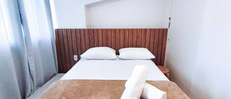A hotel room with a wooden headboard, a bed with white linens, and a rolled towel on the bed.