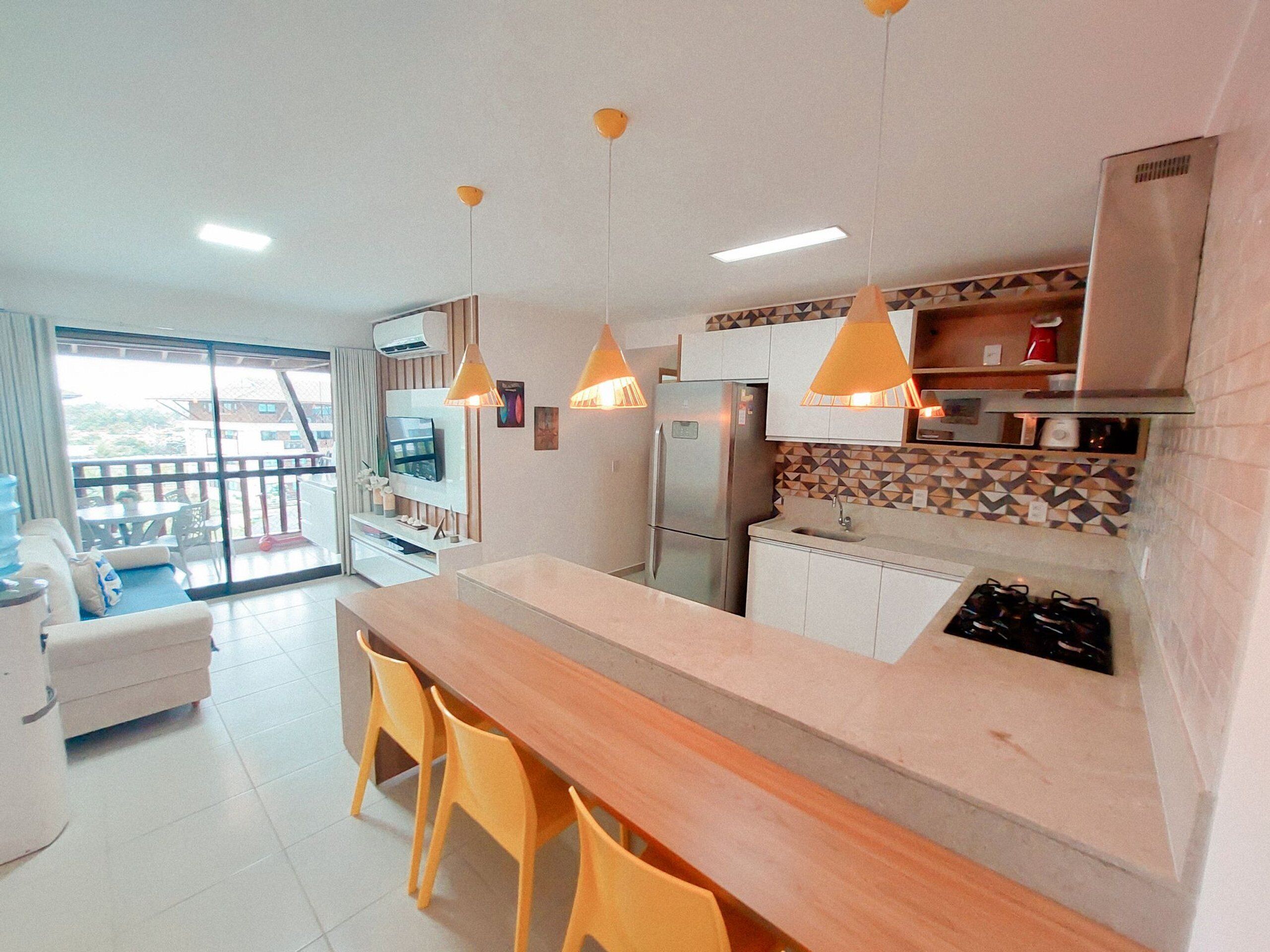 Una cocina moderna con encimera de madera, sillas amarillas, un refrigerador y luces colgantes.