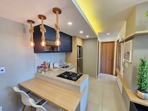 Una cocina moderna con una isla central, luces colgantes, un refrigerador y un comedor con sillas.