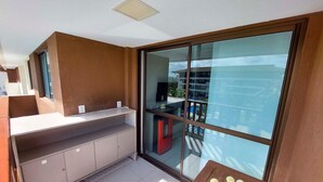 A modern kitchen with a built-in counter and cabinets, a large sliding glass door leading to an outdoor area, and a small table with a vase of flowers. - Flats no Cupe Beach Living (Ipojuca)