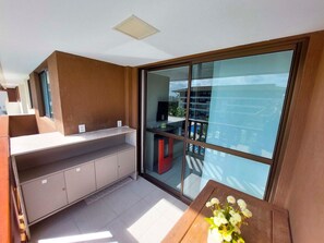 A modern kitchen with a built-in counter and cabinets, a large sliding glass door leading to an outdoor area, and a small table with a vase of flowers. - Flats no Cupe Beach Living (Ipojuca)