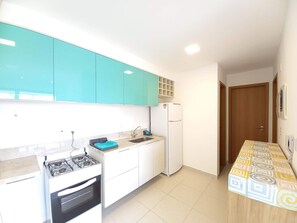 Una cocina con gabinetes azul verdoso, un refrigerador blanco, una estufa a gas y una encimera con estampado.