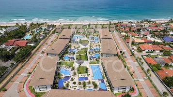 Eine Luftaufnahme eines Resorts mit mehreren Schwimmbecken, direktem Strandzugang und Wohnhäusern.