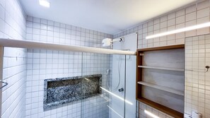 Una ducha con puerta de cristal, paredes de azulejos blancos y encimera de granito.