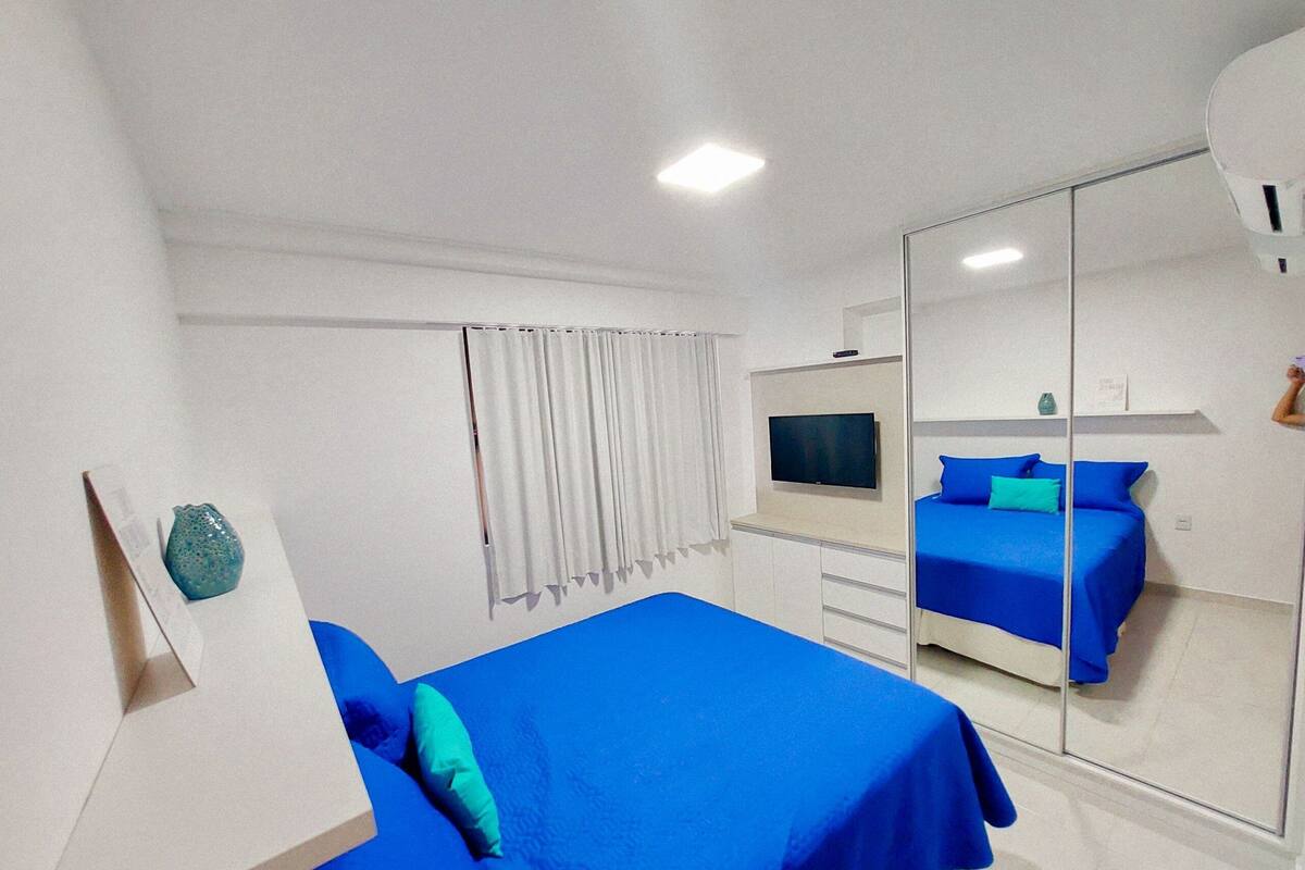 Ein Hotelzimmer mit Bett, Fernseher, Spiegel und einem Fenster mit Vorhängen.