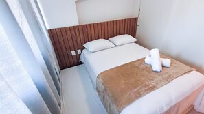 A hotel room with a bed, a wooden headboard, a white pillow, a brown throw blanket, and a rolled towel on the bed. - Flats no Cupe Beach Living (Ipojuca)