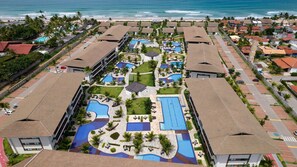 An aerial view of a resort with multiple swimming pools, a beach, and a parking area. - Flats no Cupe Beach Living (Ipojuca)