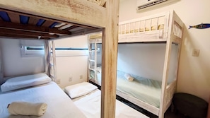 Habitación pequeña con dos literas, una ventana con persianas, un taburete y un aire acondicionado instalado en la pared.