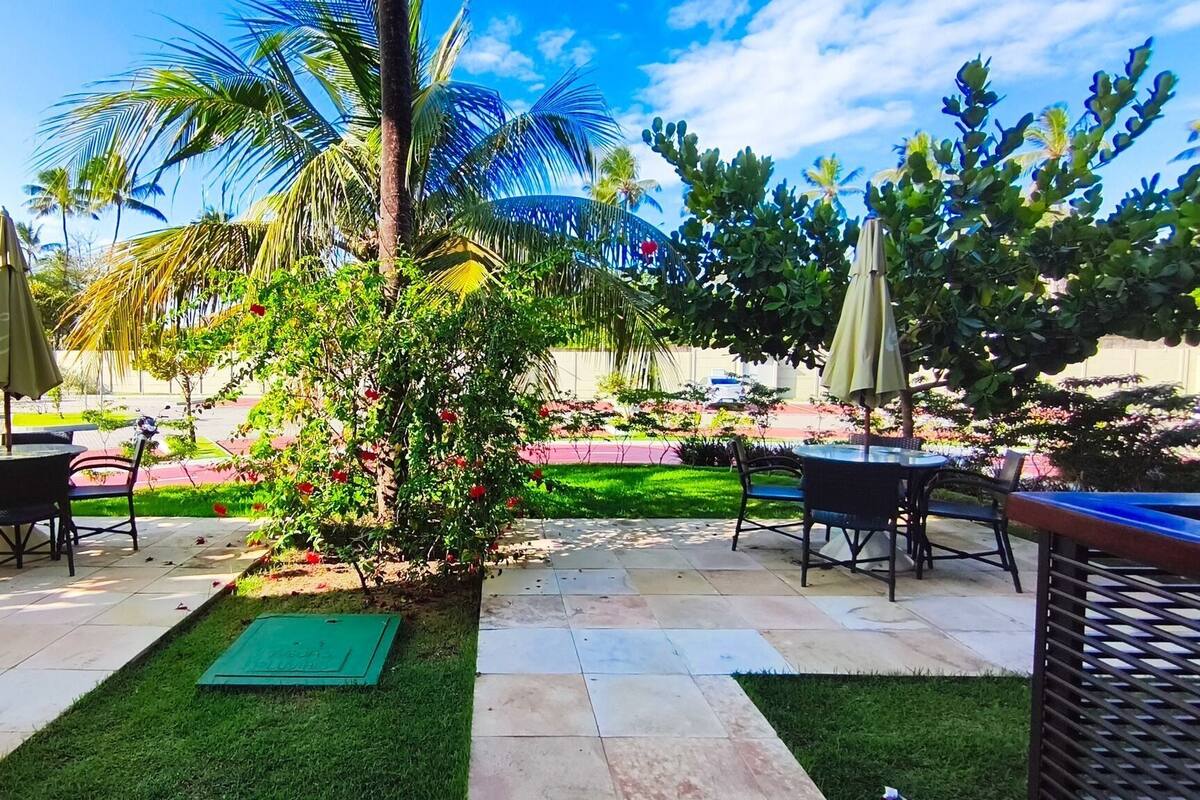 Un patio al aire libre con mesas y sillas, rodeado de abundante vegetación y palmeras.
