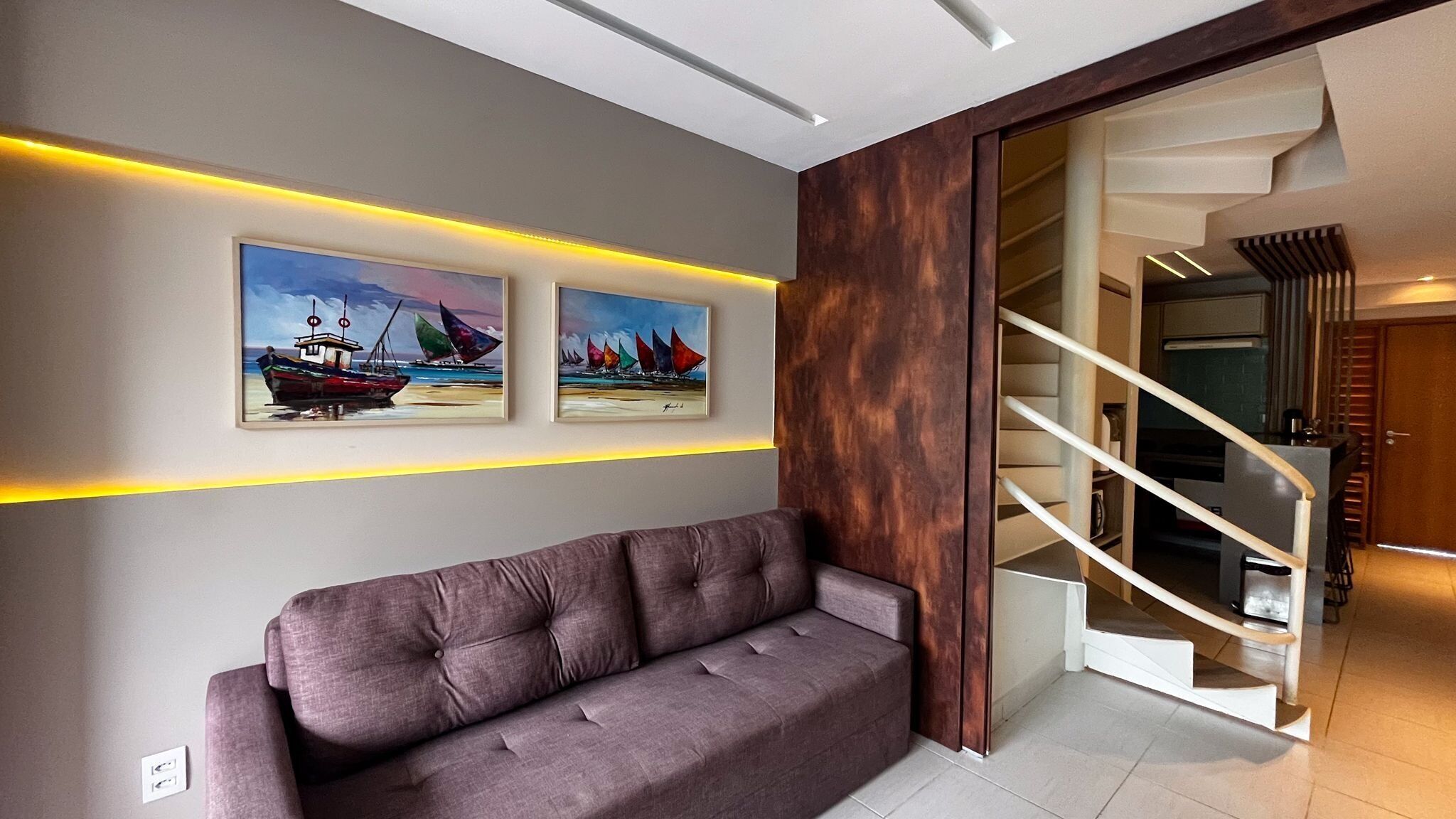 A modern living room with a sofa, two paintings, and a staircase.