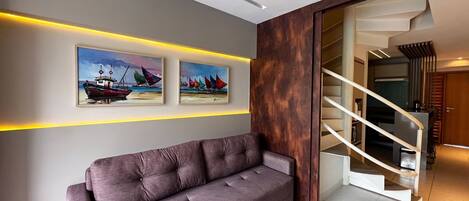 A modern living room with a sofa, two paintings, and a staircase.