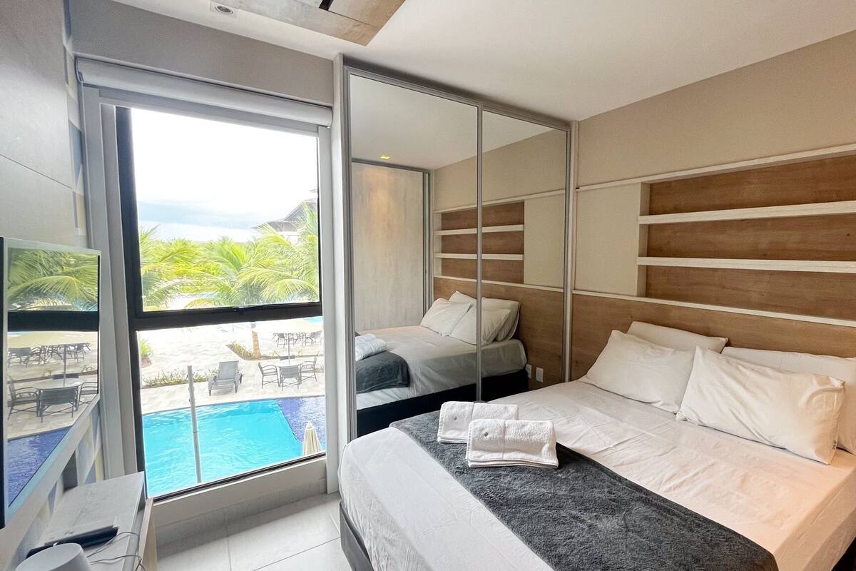 Ein Hotelzimmer mit Bett, großem Fenster und Blick auf einen Pool.