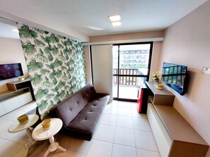 Una sala de estar con un sofá, dos mesitas, un televisor y un balcón con vistas a edificios.
