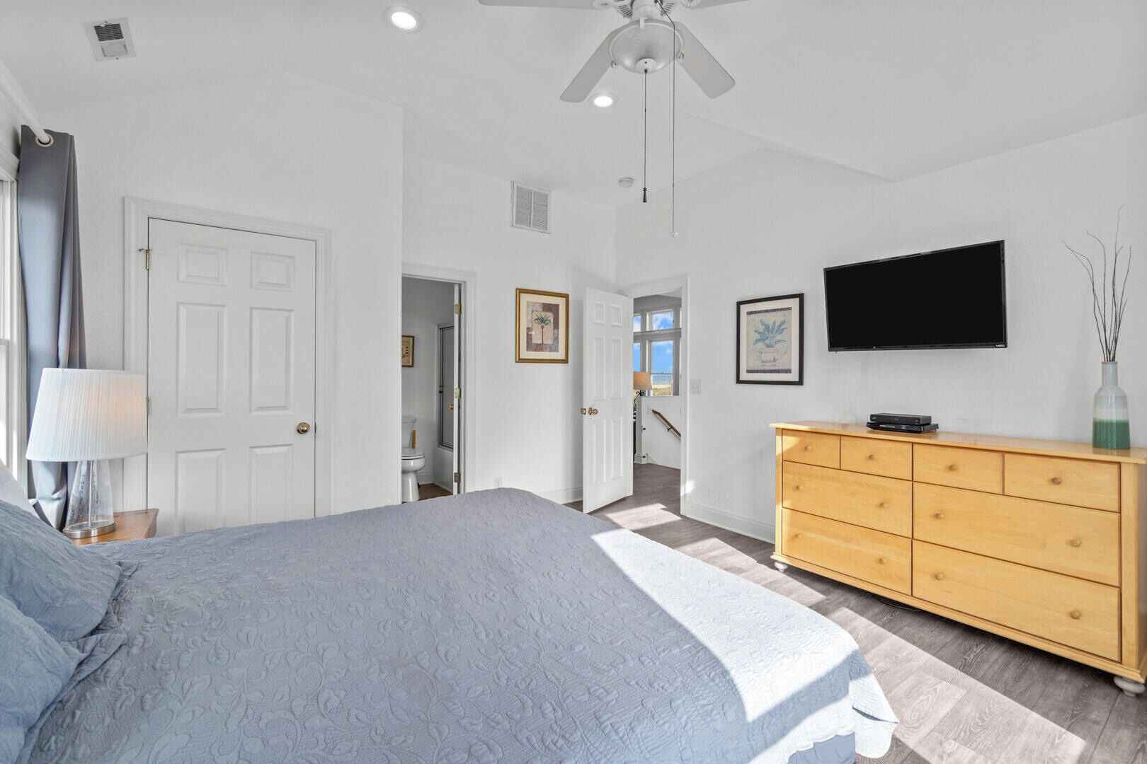 A bedroom with a bed, a dresser, a television, and a door leading to another room.
