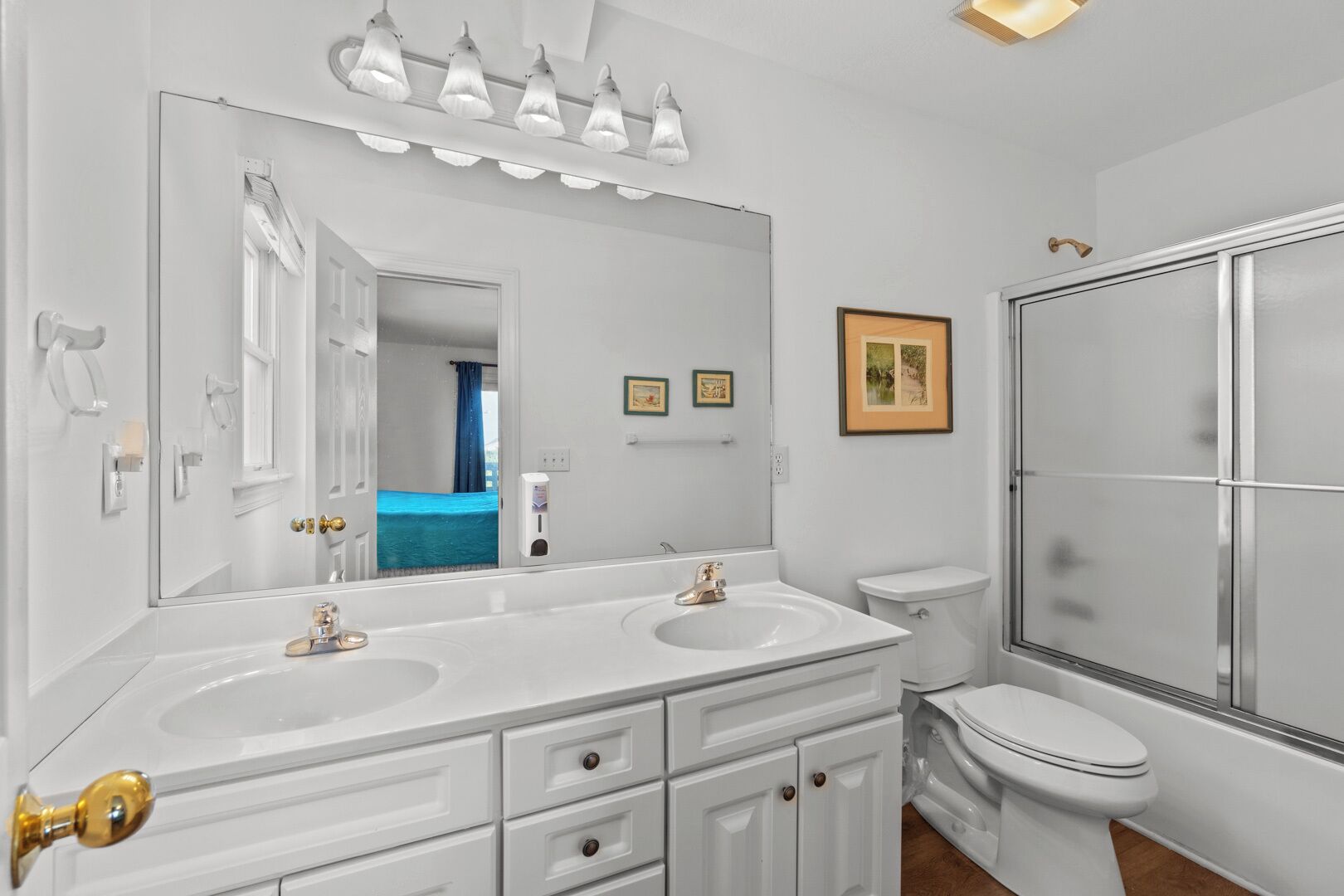 A bathroom with two sinks, a large mirror, a toilet, and a shower.