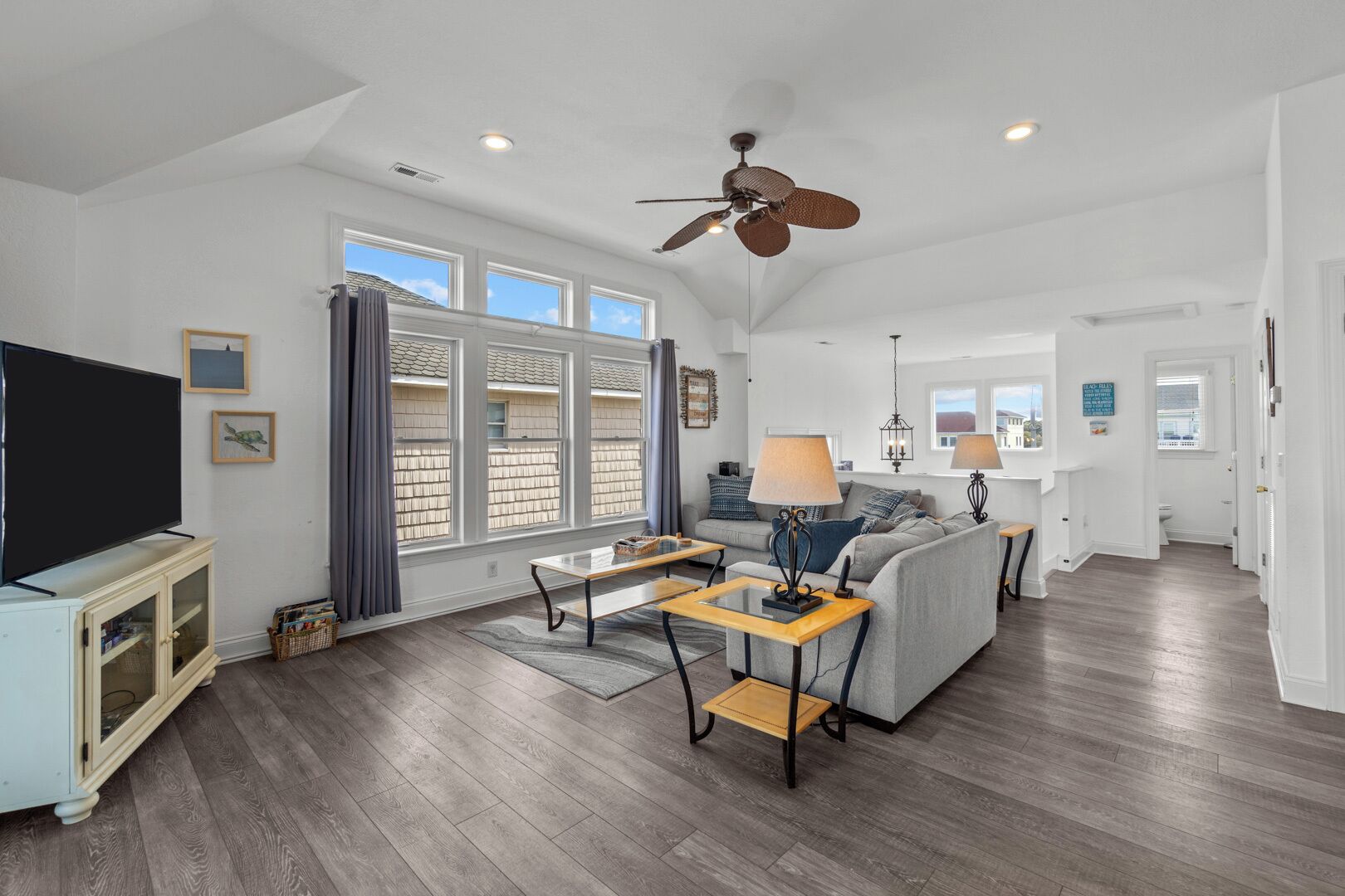 A spacious living room with a large window, a ceiling fan, and a television on a cabinet.