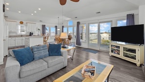 A spacious living area with a grey sofa, a coffee table, a TV, and a ceiling fan. - Paws n Relax 4 Bedroom Home With Private Pool (Kitty Hawk)