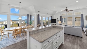A spacious kitchen with a large island, dining area with wooden chairs, and a view of the ocean. - Paws n Relax 4 Bedroom Home With Private Pool (Kitty Hawk)