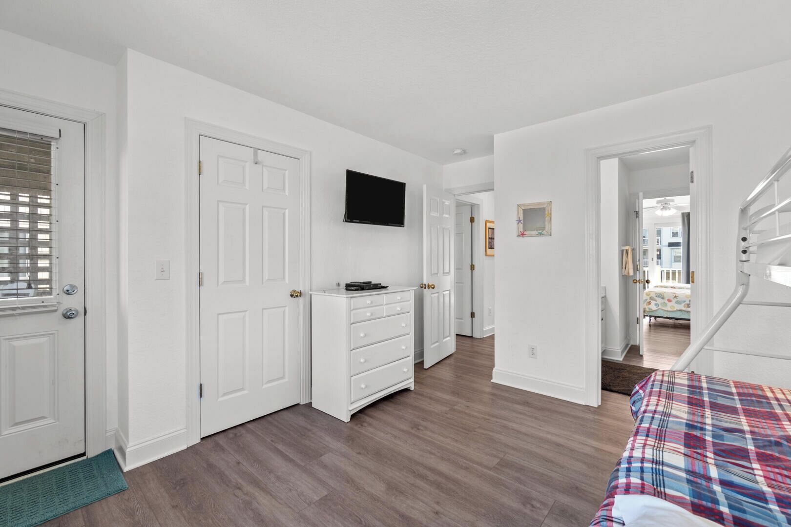 A bedroom with a bed, a dresser, a television, and a door leading to another room.