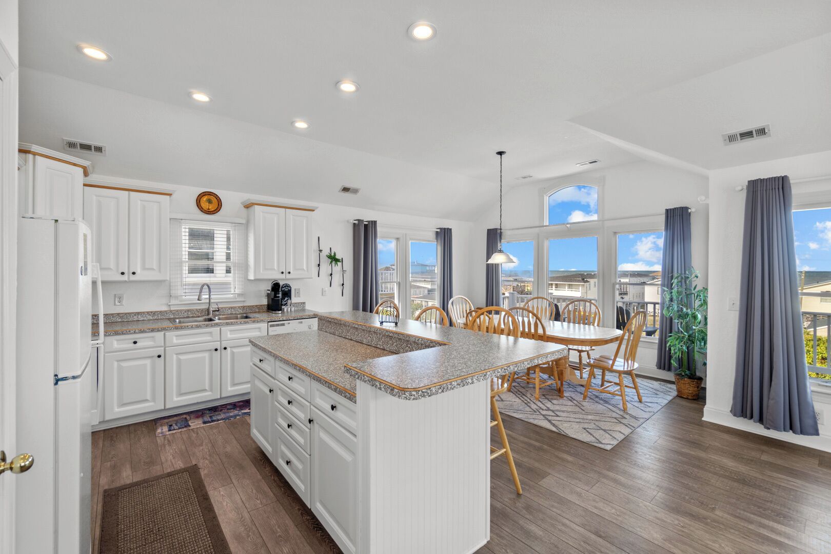 A modern kitchen with white cabinetry, a granite countertop island, and a dining area with wooden chairs.