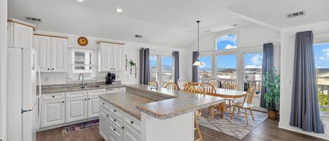A modern kitchen with white cabinetry, a granite countertop island, and a dining area with wooden chairs.