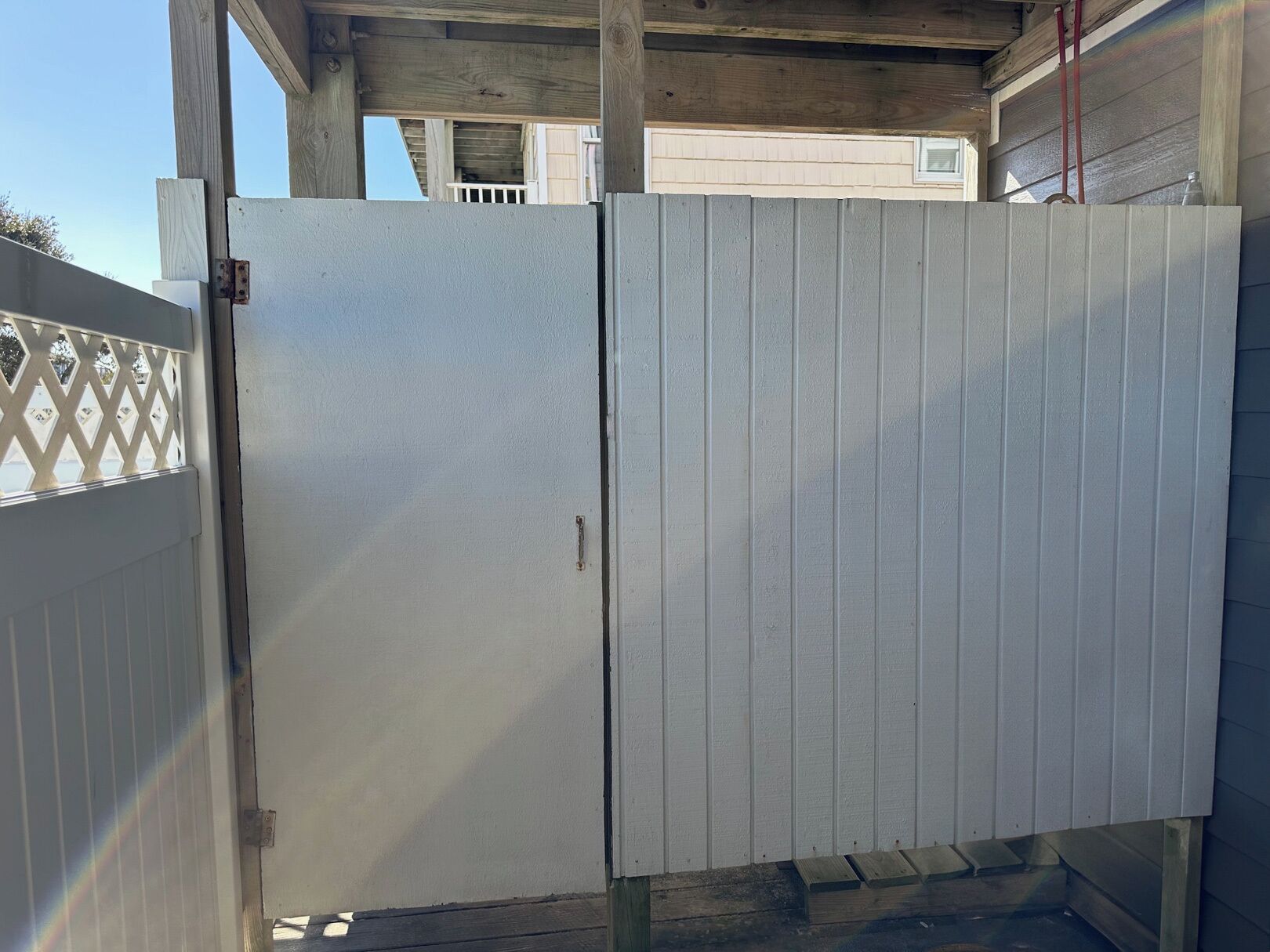 A metal gate with a latch, attached to a wooden structure with a lattice fence.