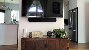 Ett modernt kök med en platt-TV som är monterad på väggen, ett träskåp under och ett kylskåp till höger.