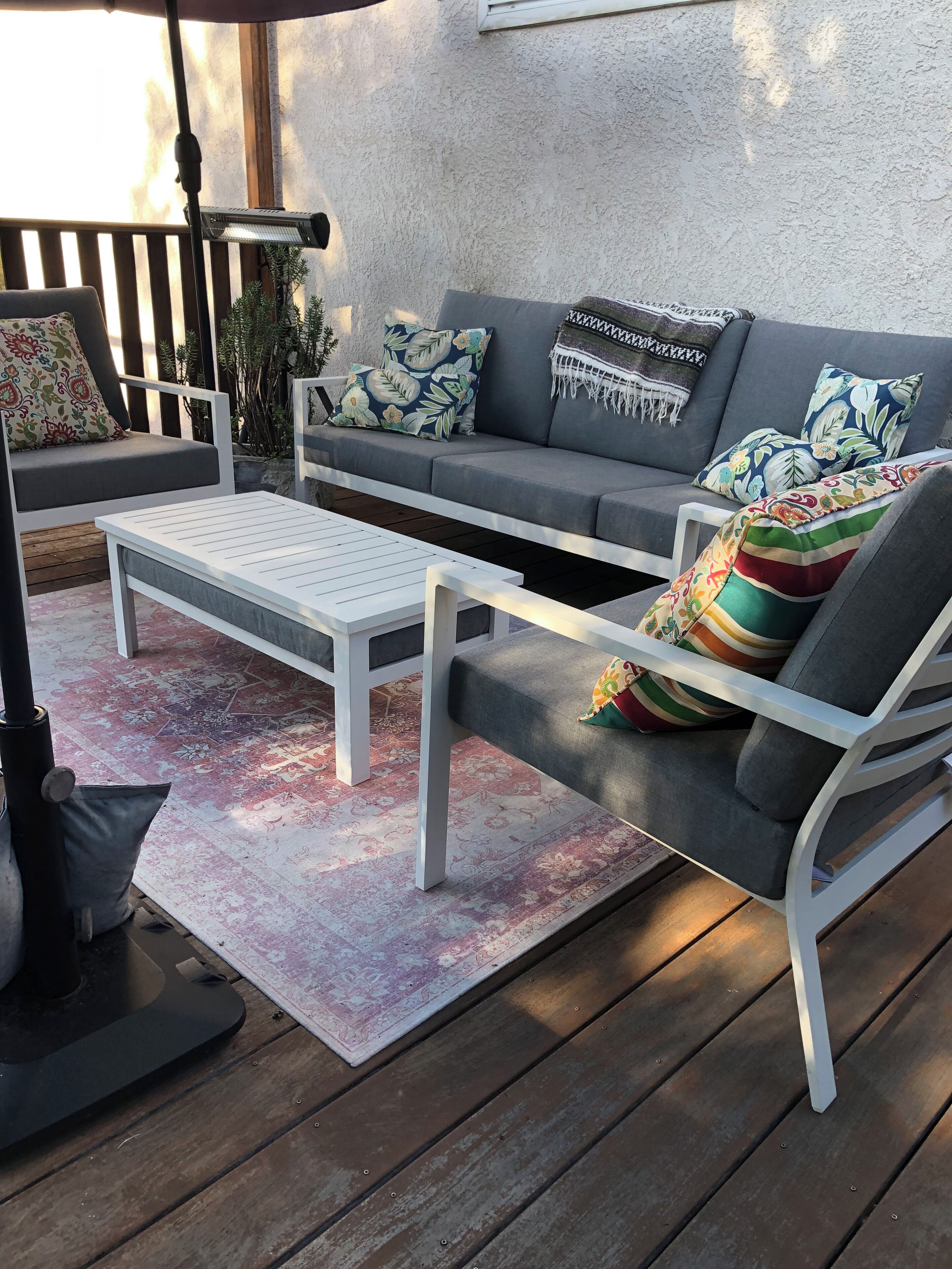 A sunlit outdoor seating area with a gray sofa, white armchairs, and a white coffee table.