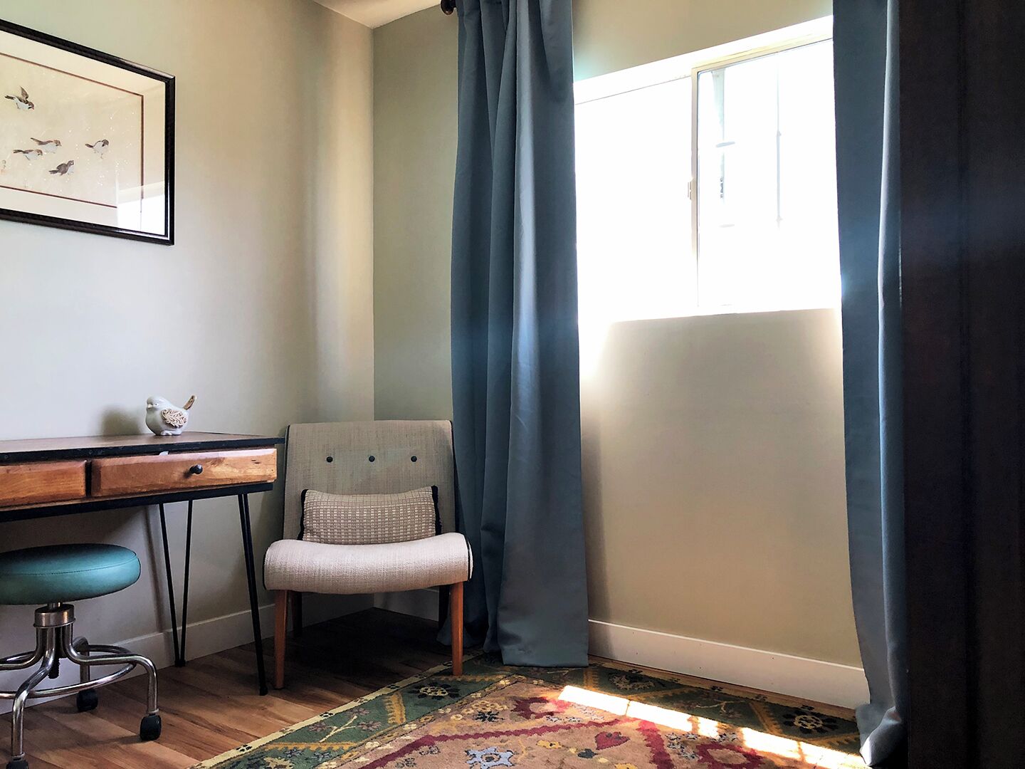 A room with a desk, chair, and a large window with curtains.
