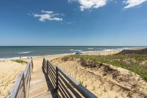 A wooden boardwalk leading to a beach with a clear sky and ocean view.