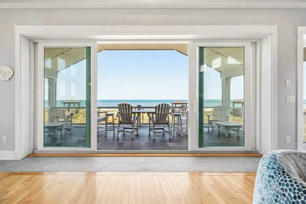 A room with a large sliding glass door leading to an outdoor patio with a view of the ocean.
