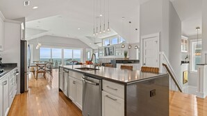 A spacious kitchen with a large island, stainless steel appliances, and a view of the ocean. - Eleanor Dare 8 Bedroom Oceanfront Home, Cabana Service, Private Pool & Pet Friendly (Nags Head)