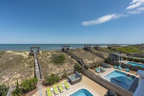 A beachside resort with a pool, lounge chairs, and wooden walkways leading to beach huts.