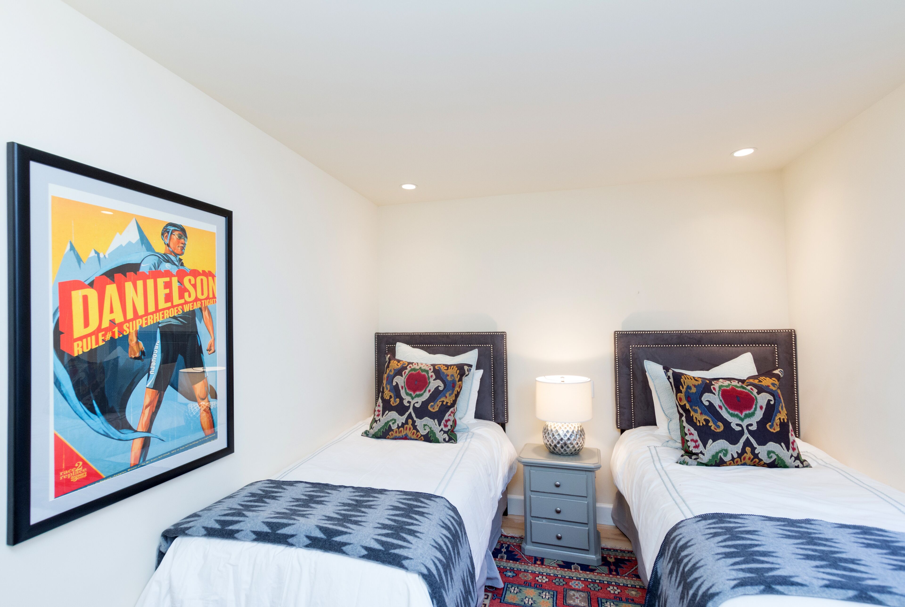 A hotel room with two beds, a nightstand, a lamp, and a framed poster on the wall.
