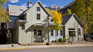 A two-story house with a garage, a chimney, and a mountain backdrop. - Christel - Peaceful West End Home, Downtown Telluride, Walk to Ski (Telluride)