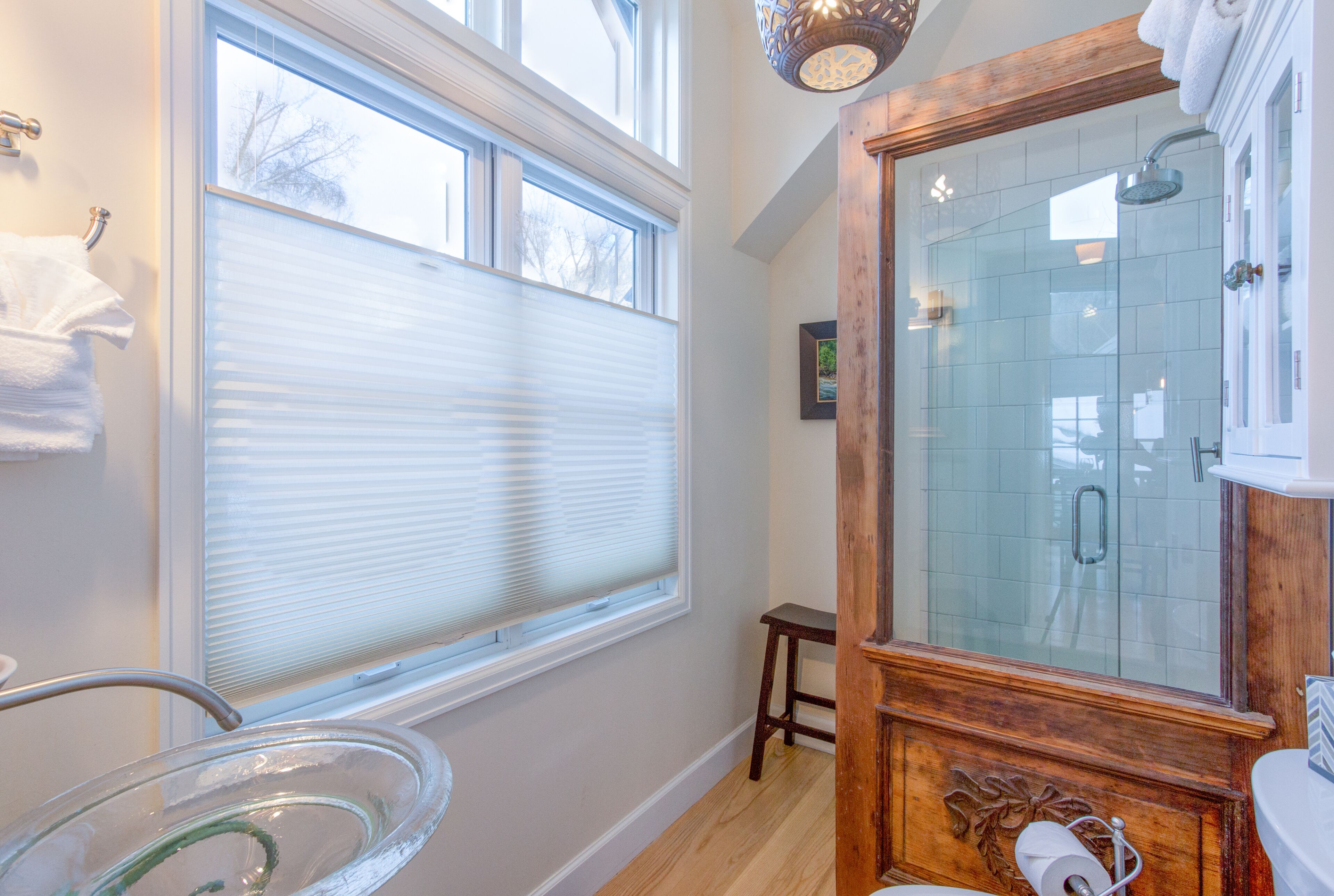 A bathroom with a glass shower enclosure, a wooden vanity, and a window with blinds.