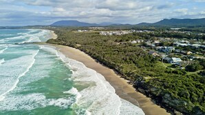 Vista aérea de una zona costera con playa, edificios residenciales y montañas al fondo.