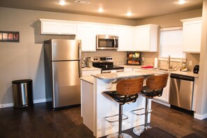 A modern kitchen with white cabinets, stainless steel appliances, and a central island with bar stools. - Close to U of A and Centennial Park (Fayetteville)